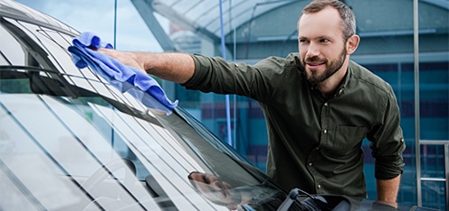 Señor limpiando con trapo azul el parabrisas de un carro gris