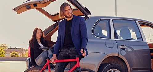 Pareja sentada en el baúl de una camioneta con una bicicleta roja al lado.